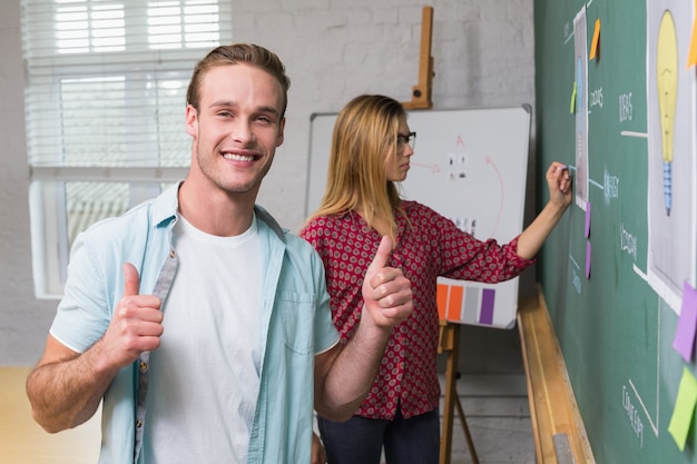 Creative business people gesturing thumbs up by blackboard