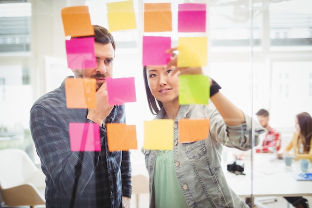 Creative business people looking at multi colored sticky notes on glass