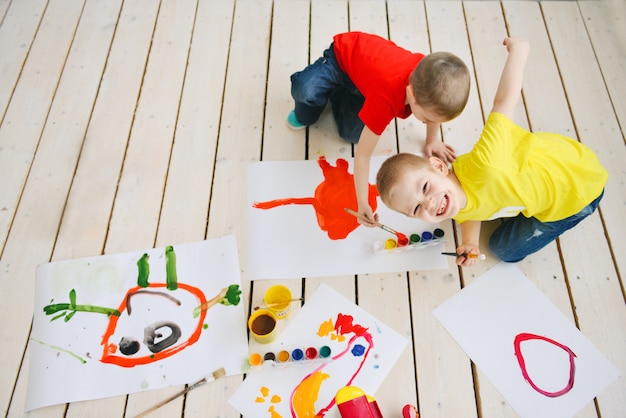 写真 創造的な子供は床に紙の面白いカラフルな写真にブラシ塗料をペイントします