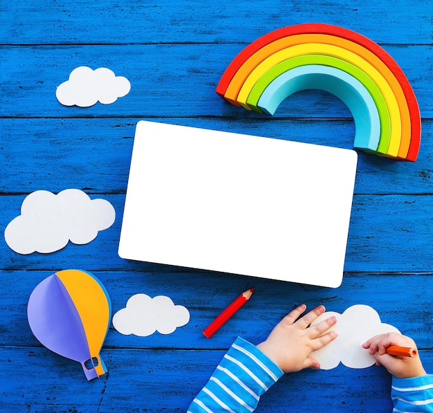 Photo creative childrens waldorf or montessori school concept paper crafts colored pencils wood rainbow and blank book with child hands on blue table kids art class kindergarten preschool background