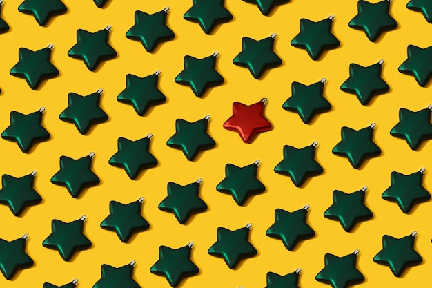写真 黄色の紙の背景に創造的なクリスマスの緑の星形のつまらない装飾パターン。最小限の新年フラットレイコンセプト。