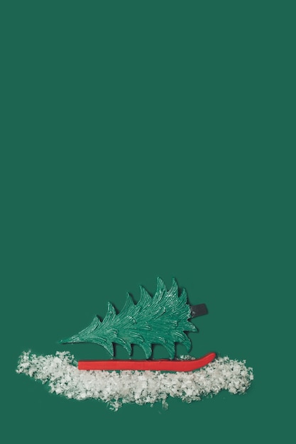 Креативный рождественский узор из зеленой игрушечной елки, белых искусственных хлопьев снега и красных лыж на зеленом фоне. Идея минимального новогоднего праздника. Обои вид сверху.