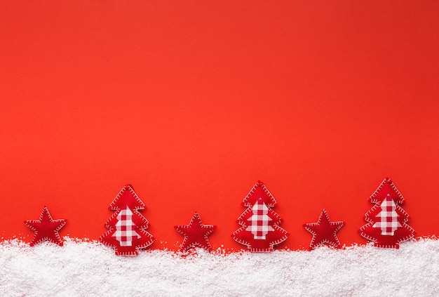 Foto reticolo di natale creativo su sfondo rosso. stella di feltro fatta a mano e alberi di natale su neve bianca, vista dall'alto, spazio di copia