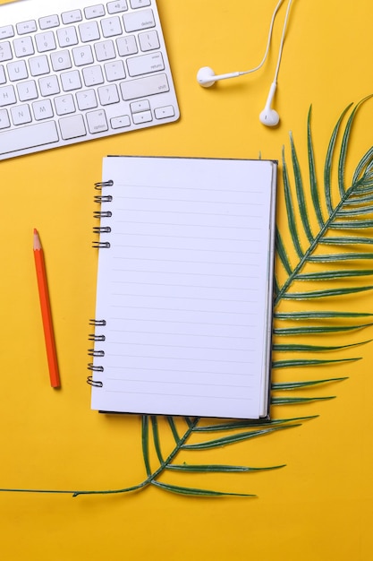 Creative composition of blank page of a notebook on palm leaf decorated with wireless keyboard earp