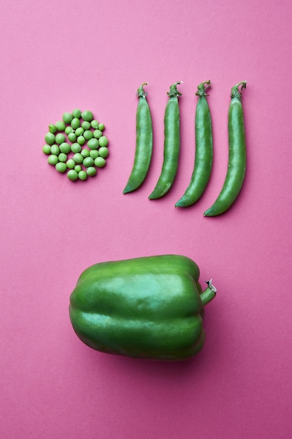 Creative composition from grains of green peas in the form of a\
circle and full of closed pods and green pepper on a pink\
background. flat lay. food concept.