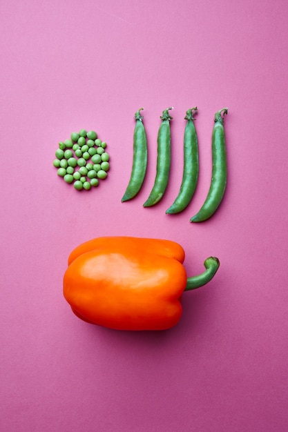 Creative composition from grains of green peas in the form of a circle and full of closed pods and red pepper on a pink background. Flat lay. Food Concept.