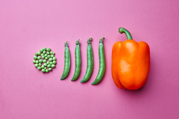 Creative composition from grains of green peas in the form of a\
circle and full of closed pods and red pepper on a pink background.\
flat lay. food concept.