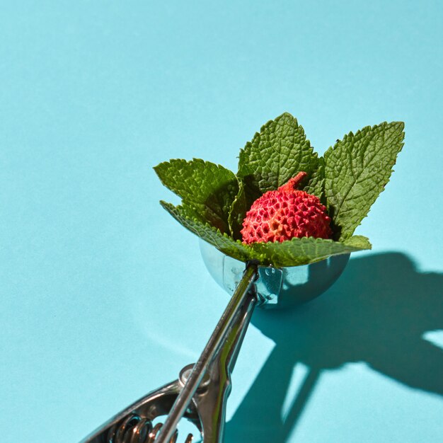 Creative composition from litchi fruit with mint leaves in the metal spoon for ice cream on a blue glass background with shadows. Food modern style.