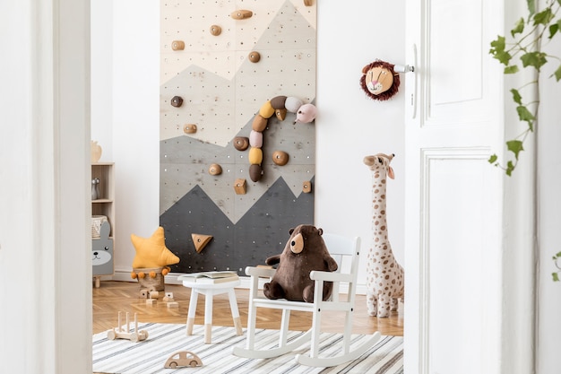 写真 スタイリッシュで居心地の良いスカンジの子供部屋のインテリアの創造的な構成壁のおもちゃとぬいぐるみのグラフィックとソファcommodeアームチェアカーペットとアクセサリー白い壁と寄木細工の床