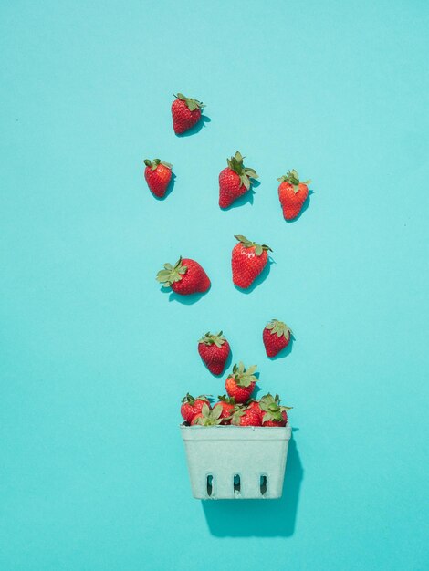 Creative composition of strawberries falling in cardboard basket for berries on a turquoise background