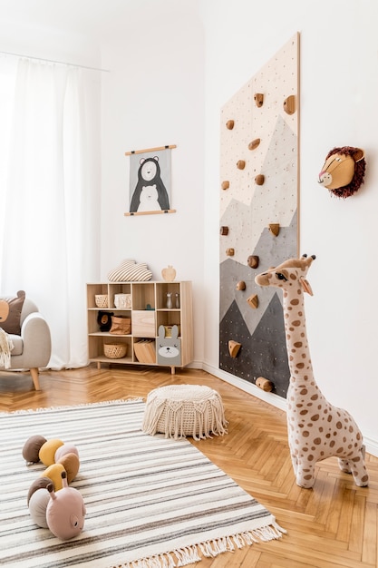 Creative composition of stylish and cozy scandi child room interior with graphic on the wall toys and plush toys sofa commode armchair carpet and accessories White walls and parquet floor