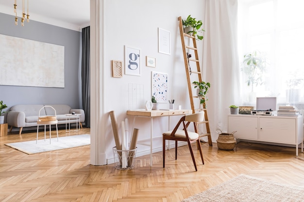 Composizione creativa dell'elegante design degli interni dell'home office scandi con cornici, scrivania in legno, sedia, piante e accessori. pareti neutre, pavimento in parquet.