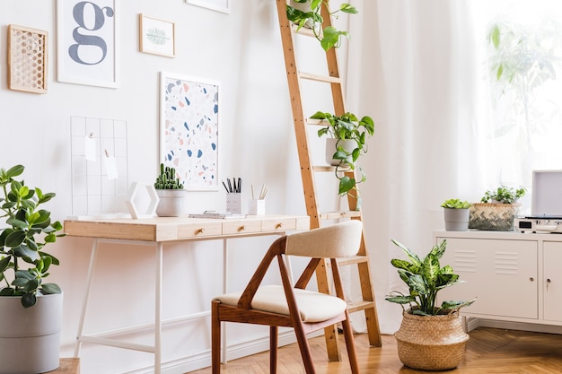 Creative composition of stylish scandinavian home office interior design with  poster frames, wooden desk, chair, plants and accessories. Neutral walls, parquet floor.