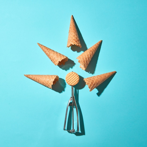 Creative composition with biscuitin the metal spoon for ice cream and waffle cones on a blue background with hard shadows. Food modern style. Top view.