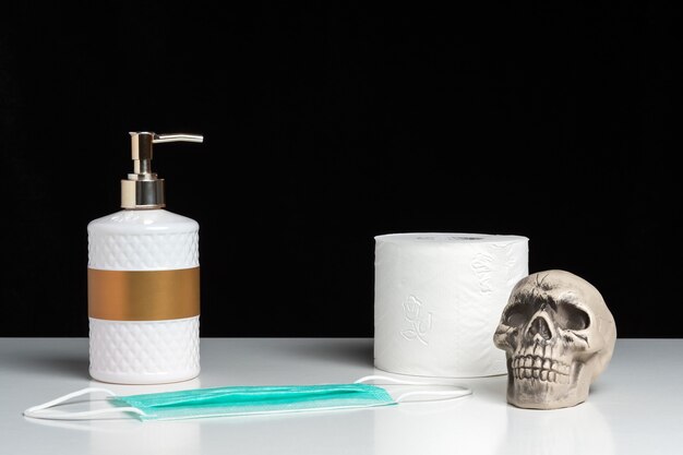 Creative composition with a hand soap and toilet paper and skull on white table.