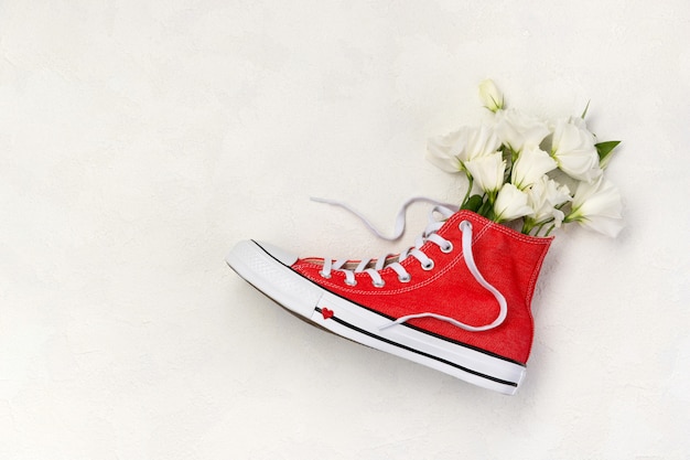 Creative composition with red sneakers and flowers on white background. Birthday woman`s day mothers day greeting card.