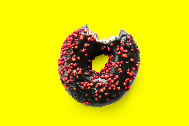 Creative concept of biting eating delicious sweet sugar black doughnut donut with red glaze bited on yellow background. Top view flat lay unhealthy dessert Food concept.