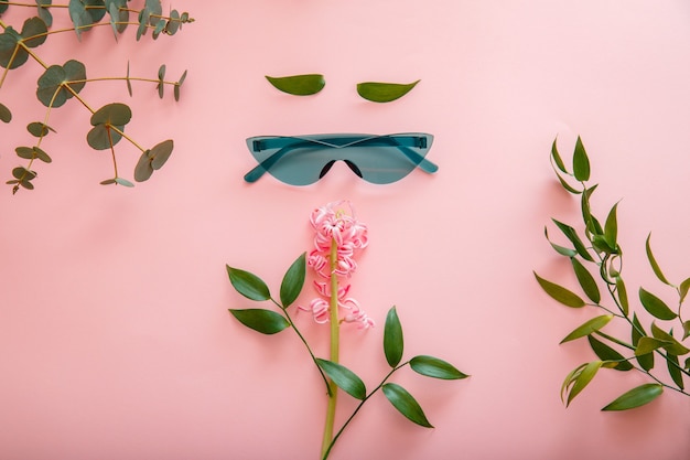 Creative concept female face made of sunglasses spring summer flowers on color summer background. Female Cartoon Face in colored green sunglasses. Top view flat lay.