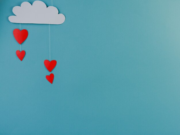 Creative concept holiday valentines day love photo of handmade paper cloud raining with hearts on blue background.