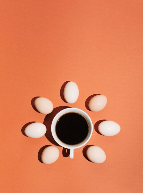 パステルブラウンオレンジの背景にコーヒーの影と卵のカップで作られた創造的なコンセプト最小限のフラットレイモックアップ