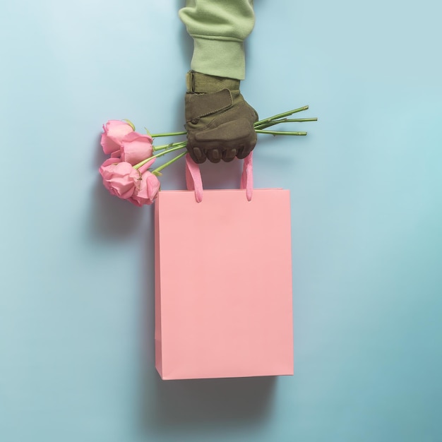 Creative concept for a men's greeting. A man's military hand holds roses with a gift bag.