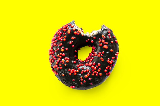 Фото Креативная концепция кусать вкусный сладкий сахарный черный пончик пончик с красной глазурью кусается на желтом фоне. плоский вид сверху лежал нездоровый десерт продовольственная концепция.