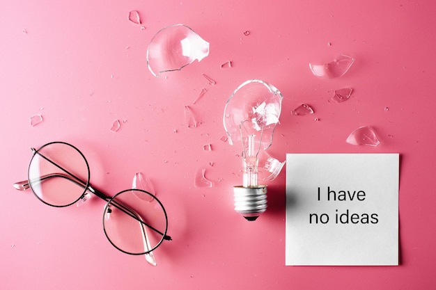 Creative crisis. Glasses and broken light bulb on a pink background. The concept of lack of ideas and inspiration.