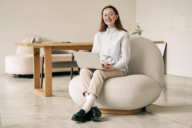 A creative designer using a laptop a smart and cheerful young woman in glasses and a blue shirt