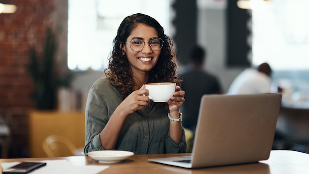 Creative entrepreneur with a laptop drinking coffee browsing internet and searching startup business ideas in cafe Portrait of smiling happy and inspired remote blogger or student with online blog