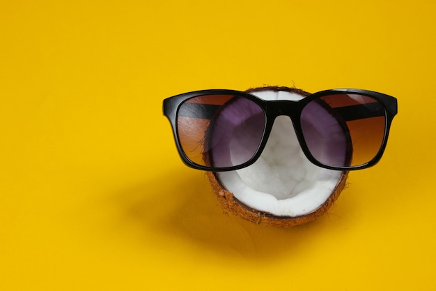 Photo creative fashion concept. coconut half with sunglasses on yellow background