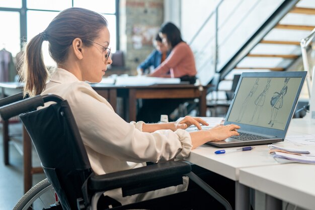 노트북 앞에서 새로운 스케치 작업을 하는 창의적인 패션 디자이너