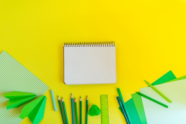 Creative, fashionable, minimalistic, school or office workspace with green supplies and spiral notebook on yellow