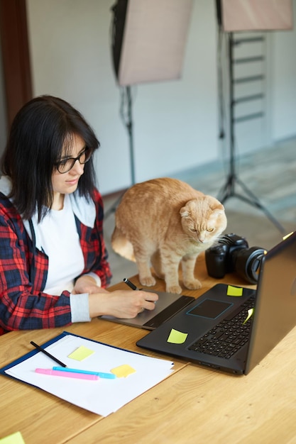 그래픽 드로잉 태블릿과 스타일러스 펜을 사용하여 귀여운 고양이를 가진 창의적인 여성 사진작가