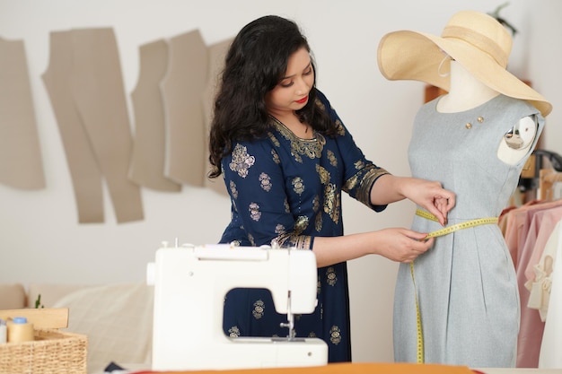 Creative female tailor measuring waist of dress on mannequin