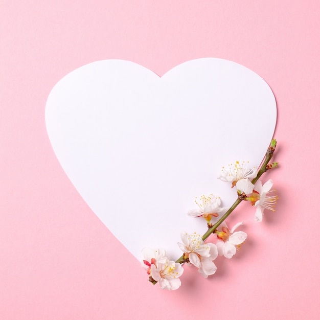 Photo creative flat lay composition: heart-shaped paper and blooming sakura branch