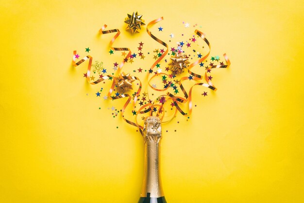 Foto composizione creativa piatta con bottiglia di champagne e spazio per il testo su sfondo colorato bottiglia di champagne con festa colorata di stelle filanti o concetto di natale