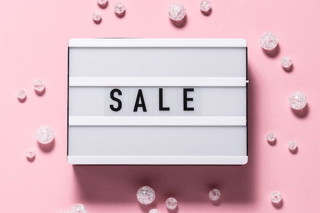 Creative flat lay overhead view of Sale text on the lightbox and shining decorations on pink background. Festive Sale and Promo concept. Black Friday