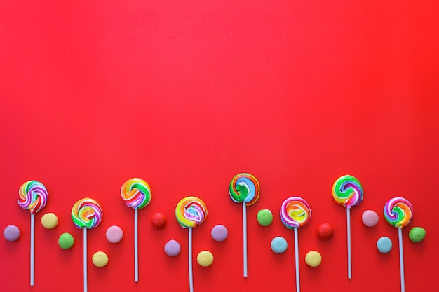 Creative flat lay of Row lollipops and chocolate candies on red background with copy space on top