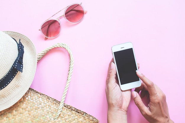 Creative flat lay of summer collection with woman hand using smartphone on colour background