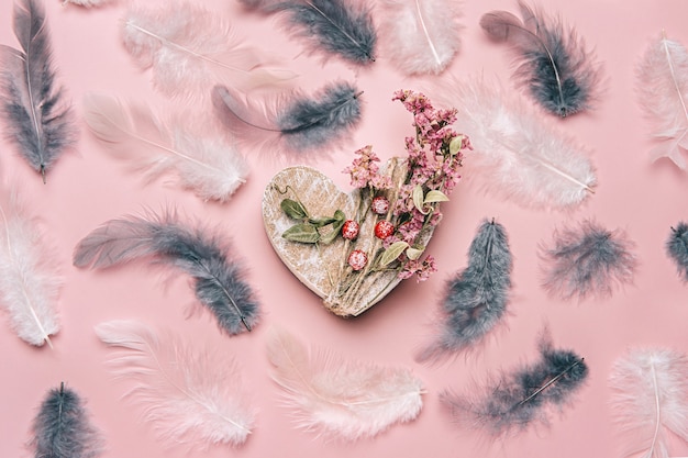 Creative flat lay of wooden heart on soft color  background with natural plants and feather.