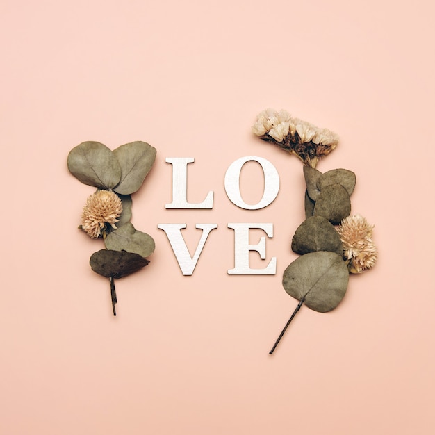 Creative flat lay of word love on soft color  background with natural plants.