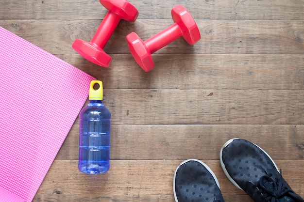 Creative flat lay of workout concept. Fitness equipment, water bottle and sport shoes on wooden floor