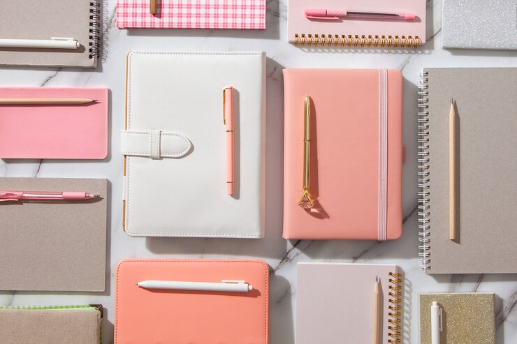 Photo creative flat lay of workspace desk with neatly arranged various coral, grey colored diary and pens.