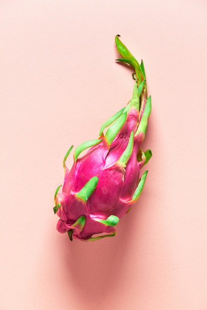 Disposizione piana creativa con dragonfruit rosa, bianco e verde organico fresco sul fondo di carta di colore di corallo. vista dall'alto alla moda, piatto disteso di tutto il frutto esotico sano maturo fresco intero.