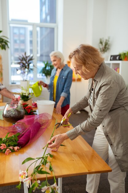 Floricoltura creativa. bella donna anziana che taglia un ramo di fiori mentre si gode la floristica