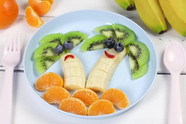 Creative food for a child kiwi tangerines and banana Fruit palms Funny food on colored utensils Fruit for a child View from above