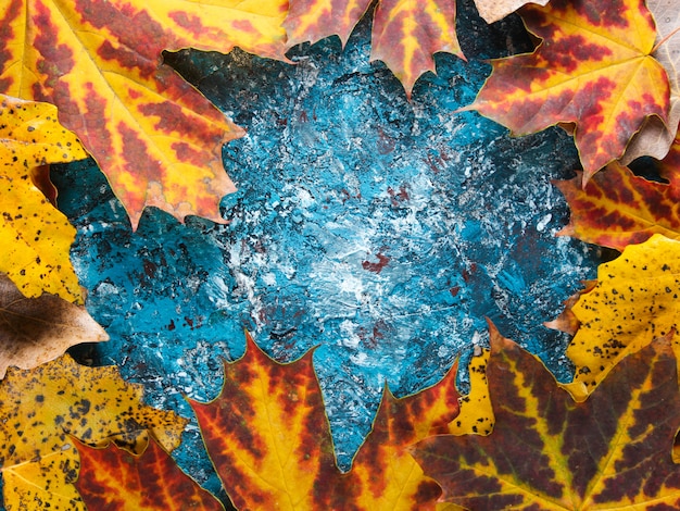 Creative frame with autumn leaves on blue concrete. Top view