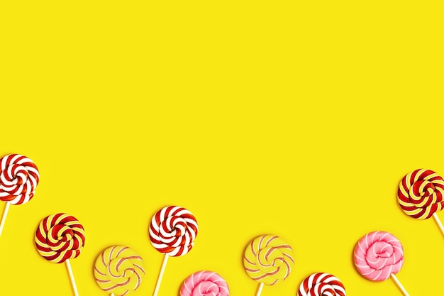 Creative frame with with sweet round candy lollypops with stripes on stick on yellow