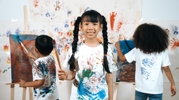 Creative girl pose at camera while diverse children painting behind erudition