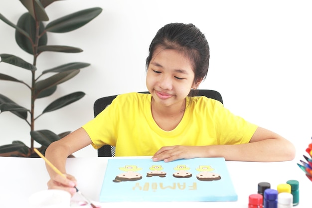 Photo creative girl sit on chair at the table drawing family picture she smiles and painting